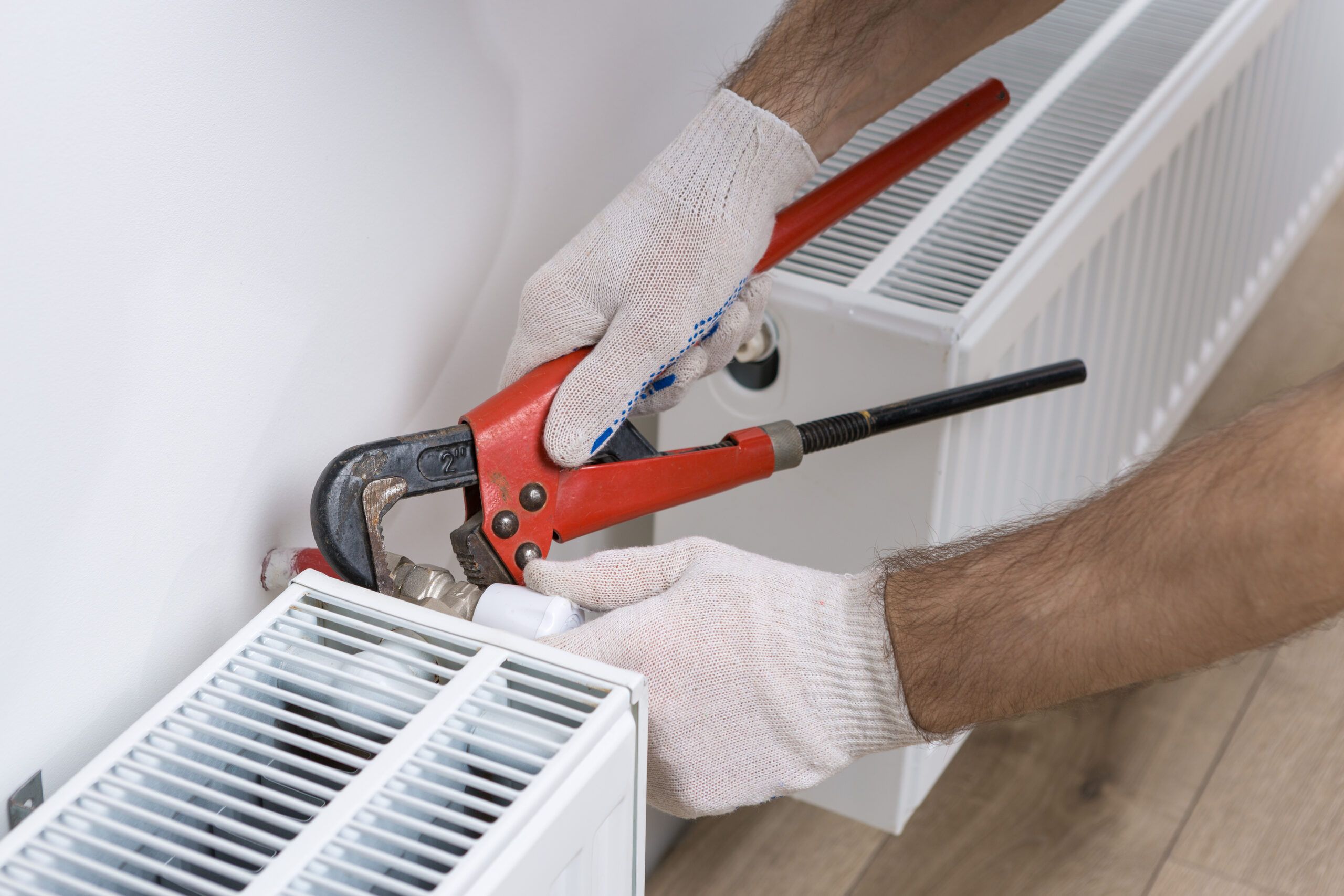 A male plumber installs a radiator in the heating system of an apartment. Guy in overalls and a gas wrench.